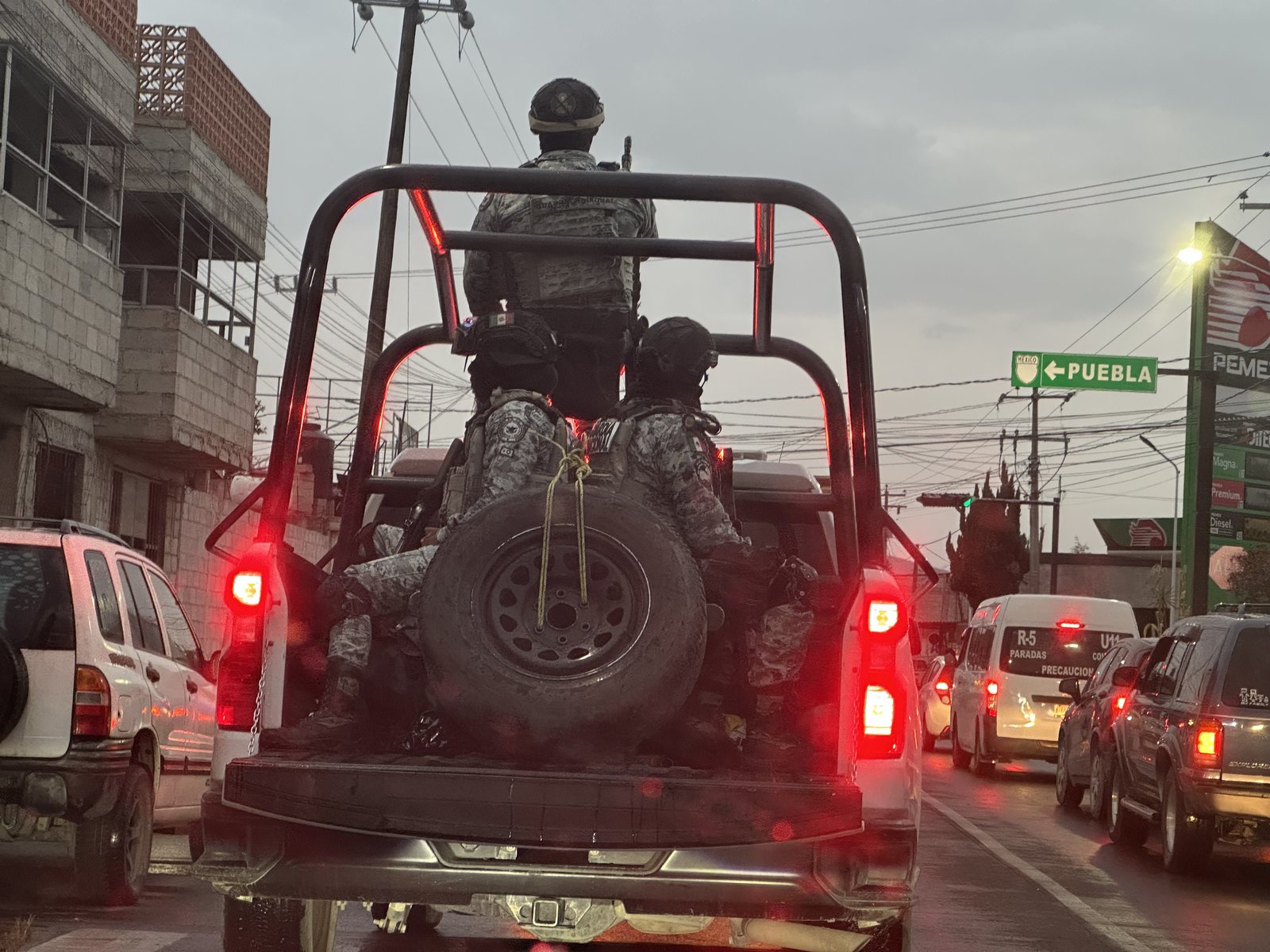 Militar sobre la caja de una camioneta entre el tráfico, al anochecer, en el entorno del tianguis de Puebla